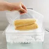 A hand is placing a vacuum-sealed bag with two ears of corn into a water bath. Produktbild-Vorschau