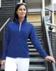 A woman wearing a blue fleece jacket and white pants stands on an outdoor staircase. Produktbild-Vorschau