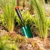 A garden trowel is stuck in the soil between tall green grass plants. Podgląd zdjęcia produktu