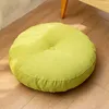 A round green floor cushion is placed on a wooden floor next to a table leg. Produktbild-Vorschau