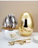 A set of cutlery in a holder and a golden egg-shaped container. Produktbild-Vorschau