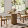A round wooden dining table with two chairs set up in a well-lit room with large windows overlooking a garden. Produktbild-Vorschau