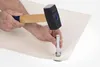 A person's hands are shown using a hammer to strike a metal punch tool onto a piece of light-colored fabric, which is likely part of a larger item or project. Produktbild-Vorschau