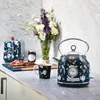 A close-up of a beautifully decorated kitchen counter featuring a floral-patterned kettle and toaster, with a small jar of jam, a slice of toast, and a mug of coffee, all arranged artfully next to a vase of fresh flowers. Produktbild-Vorschau