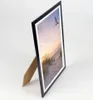 A black picture frame with a beach scene is displayed on a white background. Produktbild-Vorschau