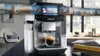 A Siemens coffee machine is shown in a modern kitchen setting, with a display showing travel images. Produktbild-Vorschau