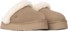 A pair of tan Ugg slippers with cream-colored trim, shown from the back. Produktbild-Vorschau