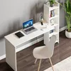 A white desk with a laptop, notebook, lamp, and coffee cup, next to a bookshelf and a chair, in a room with a grey wall and wooden floor. Voir les images du produit