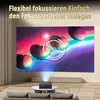 A projector is set up in a living room, projecting an image onto a large screen. The projector is placed on a coffee table in front of a sofa. The room has a modern and comfortable aesthetic. Anteprima dell’immagine prodotto