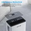 A white dehumidifier with a black top panel displaying digital readouts and touch controls, placed on a tiled floor next to a sofa. Produktbild-Vorschau