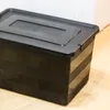 A black storage box with a lid on a wooden floor. Anteprima dell’immagine prodotto