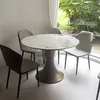 A round dining table with four chairs in a bright room with a large window overlooking greenery. Produktbild-Vorschau