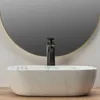 A close-up shot of a white marble oval basin with a black faucet in front of a round mirror. Anteprima dell’immagine prodotto