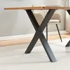Close-up of the X-shaped legs of a dining table, with a chair visible in the background. Voir les images du produit