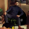 A man is sitting on a bean bag chair with a dinosaur print, with a smaller pouf in front of him. The setting appears to be an indoor lounge area with plants and furniture. Náhľad obrázku produktu