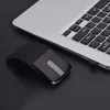 A black wireless mouse is placed next to a silver laptop on a black surface. Náhľad obrázku produktu