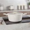 A cream-colored pot with a glass lid and gold accents sits on a black stovetop. Produktbild-Vorschau