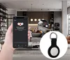 A hand holding a smartphone displaying an app, with a close-up of a keychain accessory in the foreground, set against a backdrop of a modern living room and kitchen. Produktbild-Vorschau
