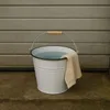 A white metal bucket filled with water and a beige cloth draped over its side, placed on a concrete surface in front of a grey ribbed garage door. Voir les images du produit