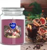 A large scented candle with a label showing mulled wine, placed next to a glass of mulled wine and festive decorations. Podgląd zdjęcia produktu