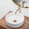 A white marble-effect round basin with a gold faucet on a wooden countertop. Produktbild-Vorschau