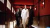 A group of people in traditional Japanese attire walking down a hallway with red walls and paper lanterns. Produktbild-Vorschau