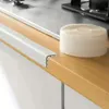 A roll of self-adhesive sealing tape and a white corner trim are placed on a wooden countertop next to a kitchen stove. Anteprima dell’immagine prodotto