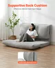A woman is sitting on a gray convertible sofa in a room with a plant. Voir les images du produit