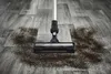 Close-up of a cordless vacuum cleaner head cleaning up spilled coffee grounds on a wood-look floor. Voir les images du produit