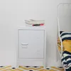 A white metal nightstand with a stack of books on top, placed next to a white metal bed frame with striped bedding. Anteprima dell’immagine prodotto
