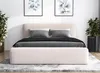 A beige upholstered bed with gray bedding and pillows, set in a room with artwork and plants.