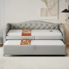 A gray upholstered daybed with a trundle pulled out, featuring two orange satin pillows. Produktbild-Vorschau