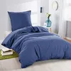 A neatly made bed with blue bedding, a pillow, and a duvet, set in a bedroom with a small table and decorations. Produktbild-Vorschau