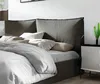 A close-up view of a bed with a gray upholstered headboard and white bedding. Produktbild-Vorschau