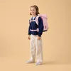 A young girl wearing a backpack and standing against a plain background. Produktbild-Vorschau
