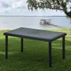 A rectangular poly rattan table with a glass top is placed on a grassy lawn next to a lake with a pier and a boathouse in the background. Anteprima dell’immagine prodotto