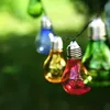 A string of colorful, illuminated light bulbs hanging outdoors against a blurred green background. Produktbild-Vorschau