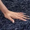 A close-up shot of a hand resting on a dark blue shaggy rug. Produktbild-Vorschau