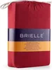 A folded red fitted sheet packaged in its own fabric bag, with a branded label wrapped around it. Produktbild-Vorschau