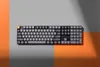 A keyboard is placed on a surface divided into gray and orange sections, with shadows cast across it. Produktbild-Vorschau