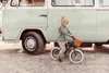 A young boy is riding a balance bike next to a vintage camper van. Produktbild-Vorschau