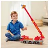 A young boy is sitting on the floor playing with a toy fire truck with a crane. Produktbild-Vorschau