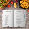 An open recipe book with a recipe for Ayurvedic soup, surrounded by ingredients and prepared food. Produktbild-Vorschau