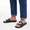 A person wearing blue jeans and black Puma slides. Anteprima dell’immagine prodotto