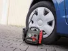A car tire is being inflated by a portable compressor. The compressor is connected to the tire valve. Anteprima dell’immagine prodotto