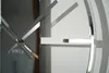 A close-up shot of a modern silver wall clock with its hands casting shadows on a white wall. Náhled obrázku produktu