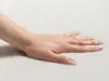 A hand resting on a soft, white surface. Produktbild-Vorschau