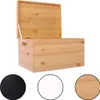 A wooden storage box with its lid open, shown against a white background. Below the box are three circular swatches representing different color options: black, white, and natural wood. Produktbild-Vorschau