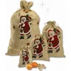 Four burlap sacks with Santa Claus designs are arranged in a group, with two tangerines and some nuts in the foreground. Produktbild-Vorschau