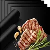 A product shot featuring grilled steaks, garlic, and rosemary on a black surface, with rolled-up grill mats in the background. Náhled obrázku produktu